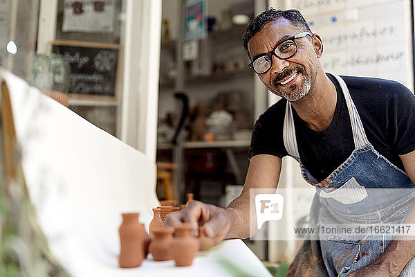 Lächelnder männlicher Töpfer mit Miniaturen auf dem Tisch in der Werkstatt