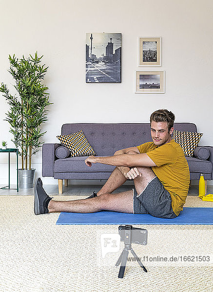 Young man watching mobile phone while exercising on mat at home