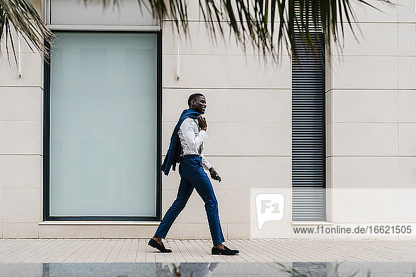 Lächelnder männlicher afrikanischer Berufstätiger  der auf dem Bürgersteig in der Stadt geht