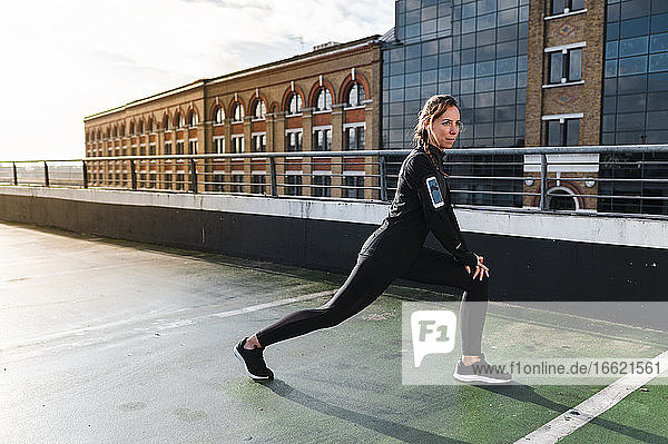 Female athlete stretching legs on rooftop against buildings in city