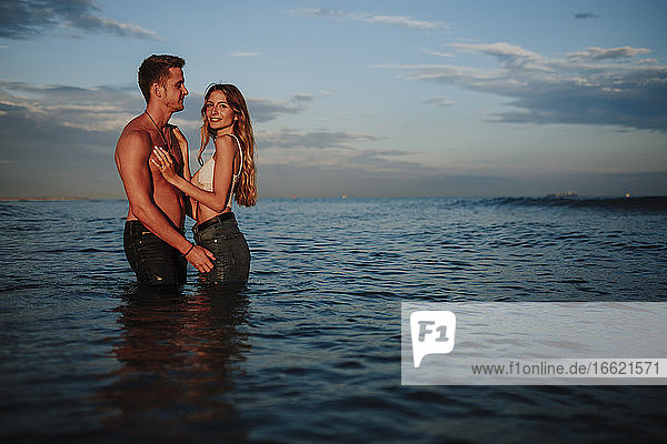 Mann und Frau stehen bei Sonnenuntergang im Wasser