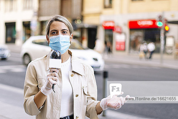Reporterin mit Maske  die über ein Mikrofon spricht  während sie auf einer Straße in der Stadt steht