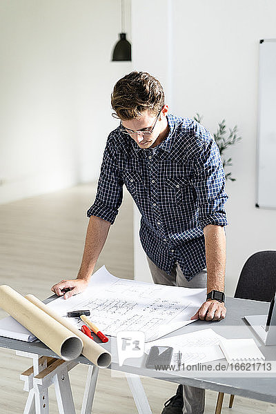 Architekt  der einen Bauplan analysiert  während er im Büro am Schreibtisch steht