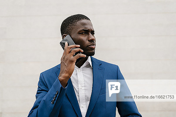 Young businessman looking away while on the phone against wall in city