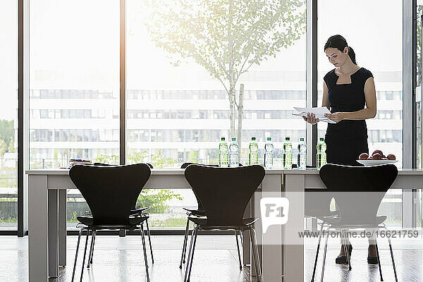 Geschäftsfrau  die Berichte analysiert  während sie am Schreibtisch vor dem Fenster im Büro steht