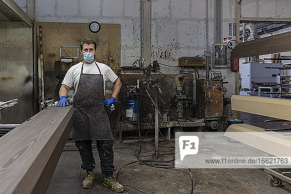 Mann mit Maske steht an einer Planke in einer Holzfabrik