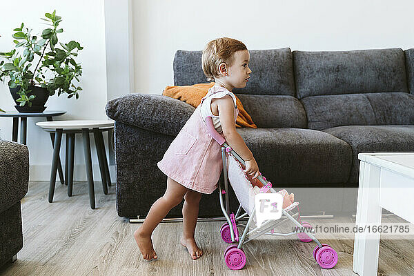 Baby girl playing with toys and baby stroller at home