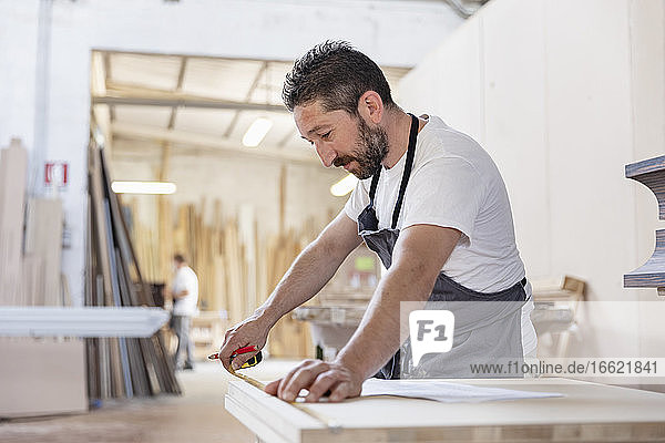 Man measuring wood with measurement tape while standing at workshop