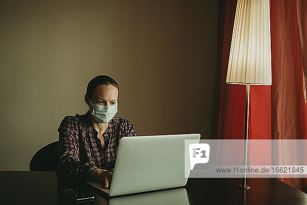 Geschäftsfrau mit Gesichtsschutzmaske bei der Arbeit am Laptop im Büro