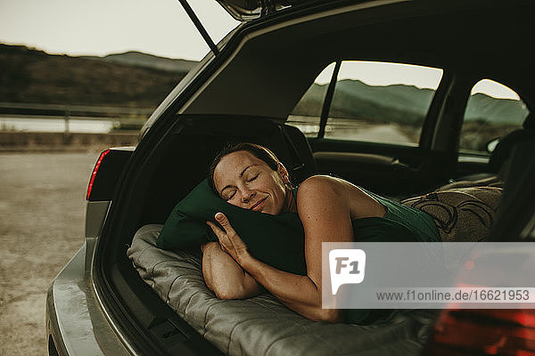 Müde Frau schläft in der Abenddämmerung im gemütlichen Kofferraum eines Autos