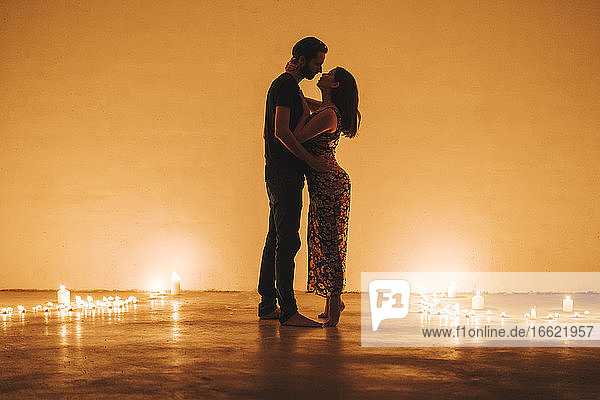 Romantisches Paar  das sich küsst und umarmt  während es inmitten von angezündeten Kerzen an der Hauswand steht