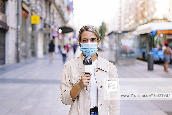 Journalistin mit Maske und Mikrofon auf der Straße in einer Stadt