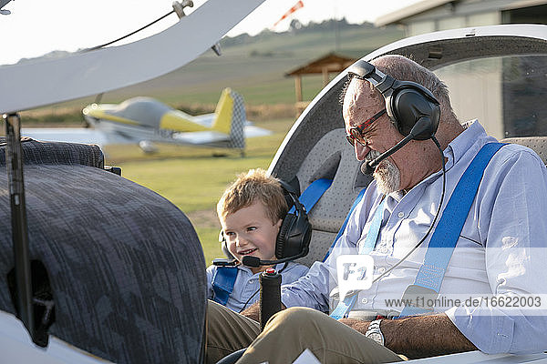 Grandson and grandfather sitting inside airplane at airfield