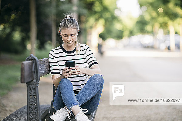 Mittlere erwachsene Frau  die ein Smartphone benutzt  während sie in einem öffentlichen Park sitzt