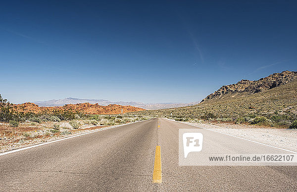 Diminishing view of empty desert road against blue sky  Nevada  USA
