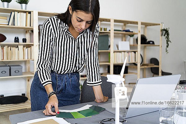 Junge Architektin bei der Auswahl eines Farbtons aus Farbmustern am Schreibtisch im Büro