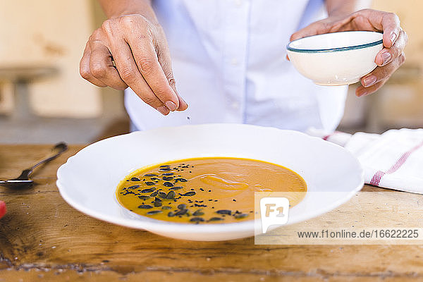 Woman putting sesame seed in soup while standing at table