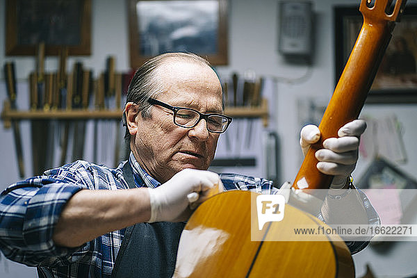 Senior men polishing guitar while standing at workshop
