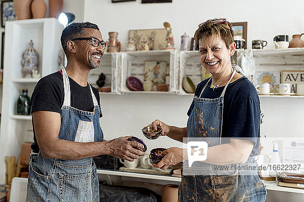 Lächelnde Künstler  die Keramik in der Hand halten  während sie in der Werkstatt stehen