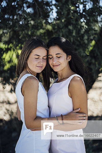 Lesbian couple with eyes closed standing against tree