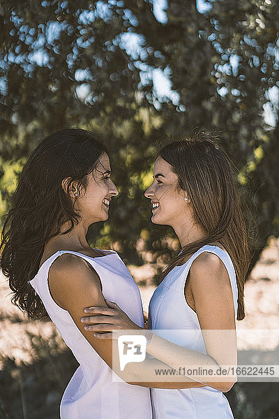 Smiling lesbian couple embracing each other while standing against tree