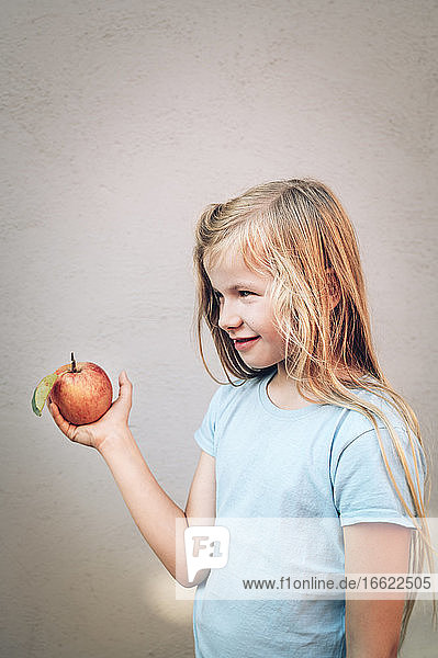 Nettes blondes Mädchen hält frischen roten Bio-Apfel an der Wand