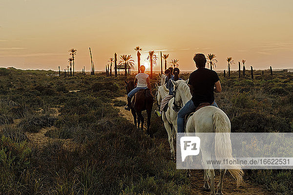 Familie reitet Pferde auf Landschaft gegen Himmel während Sonnenuntergang