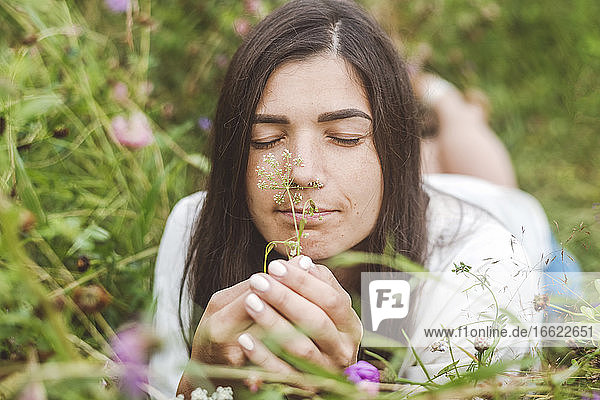 Close-up of mid adult woman with eyes closed smelling flowers while lying on land