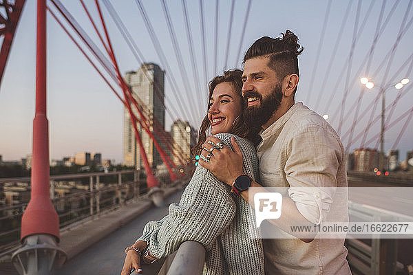 Fröhlicher Freund und Freundin stehen bei Sonnenuntergang auf einer Brücke in der Stadt