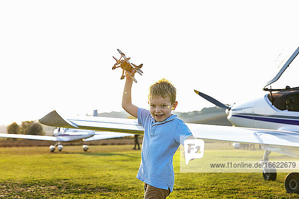 Niedlicher kleiner Junge  der mit einem Spielzeugflugzeug spielt  während er auf dem Flugplatz steht