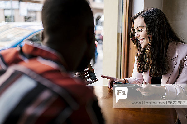 Junger Mann zeigt seiner Freundin das Smartphone  während er im Café sitzt