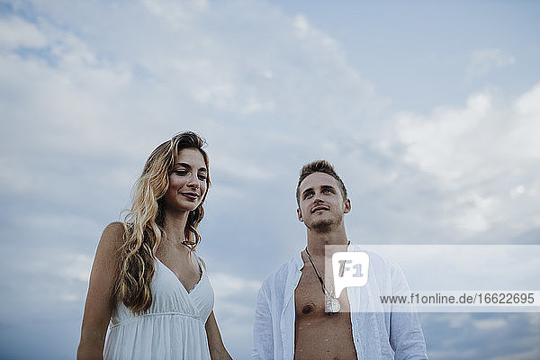 Smiling man and woman looking away while standing against sky