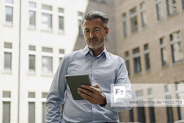 Businessman using digital tablet while standing against building