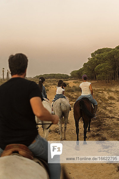 Family riding horses on landscape against clear sky during sunset