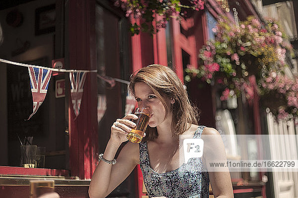 Frau trinkt Bier  während sie an einem sonnigen Tag vor einer Kneipe sitzt