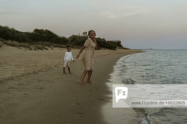 Großmutter und Enkel stehen am Strand bei Sonnenuntergang