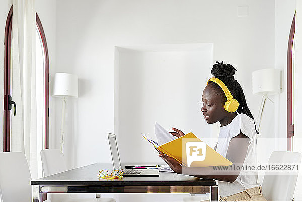 Geschäftsfrau mit Kopfhörern beim Lesen eines Buches am Schreibtisch im Heimbüro