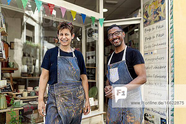 Lächelnde Mitarbeiter mit Schürzen stehen vor einem Keramikgeschäft
