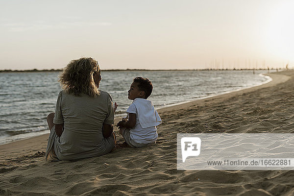 Großmutter und Enkel unterhalten sich am Strand bei Sonnenuntergang miteinander