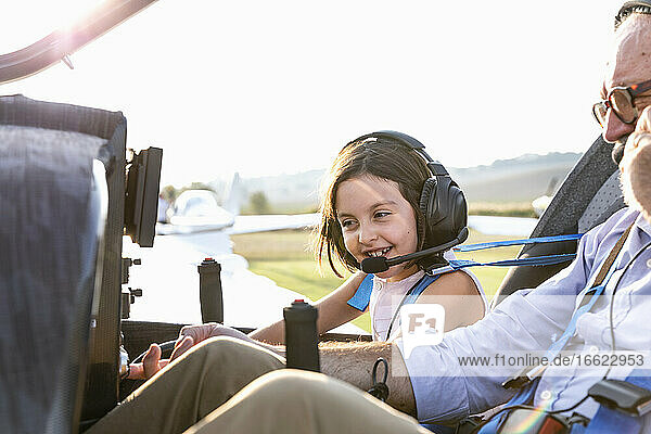 Kleines Mädchen im Cockpit eines Flugzeugs mit Großvater auf einem Flugplatz an einem sonnigen Tag
