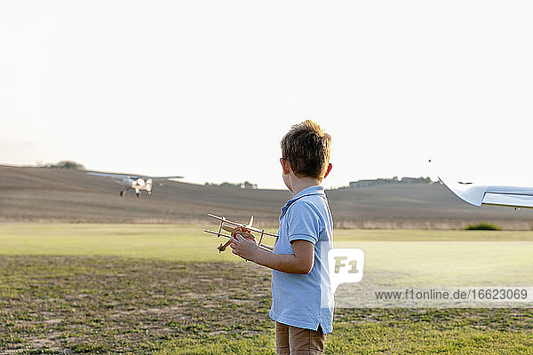 Little boy holding toy airplane while standing at airfield