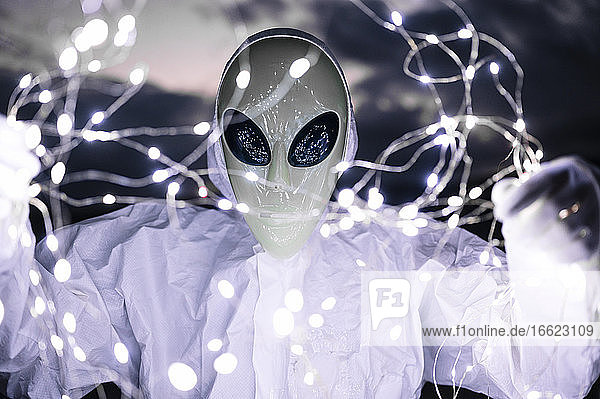 Man in alien costume holding illuminated string lights at dusk