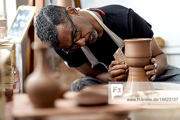 Nahaufnahme eines männlichen Künstlers bei der Herstellung von Steingut auf einer Töpferscheibe in einer Werkstatt