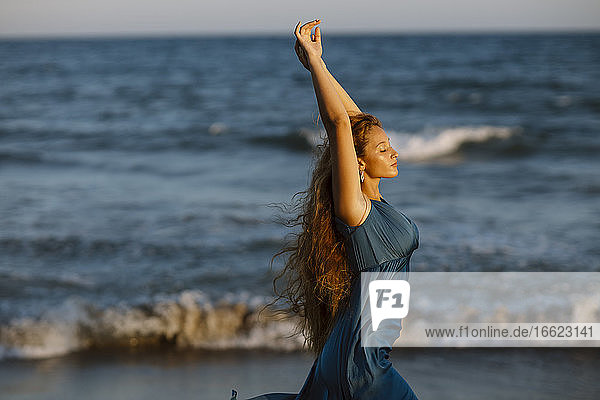Schöne Frau mit erhobener Hand tanzt im Stehen gegen das Meer