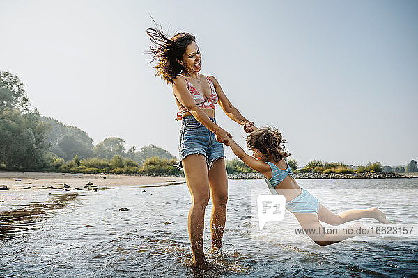 Mother whirling daughter around while standing in water at beach