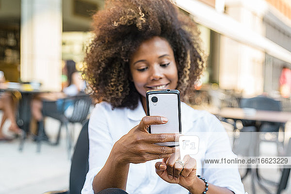 Woman taking selfie on smart phone while sitting at sidewalk cafe