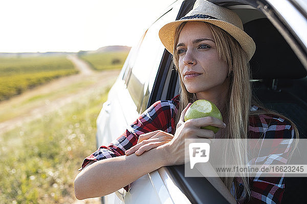 Junge Frau isst Obst  während sie im Auto sitzt