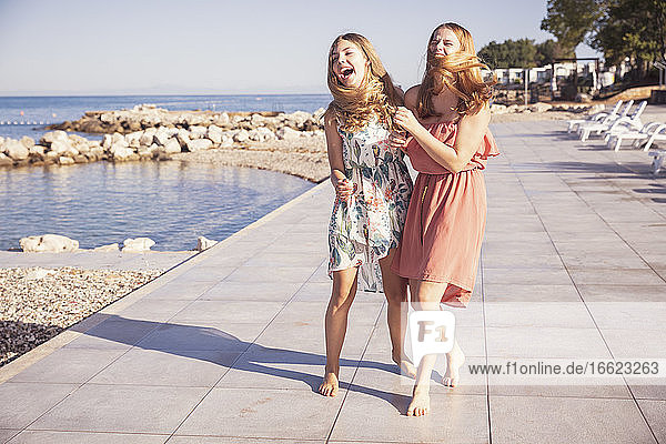 Weibliche Freunde gehen auf dem Bürgersteig gegen das Meer an einem sonnigen Tag