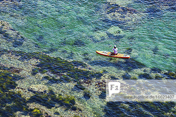 Aerial view of woman paddleboarding in clear water of Lukin bay