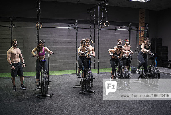Frauen  die auf einem Fitnessrad trainieren  während Männer im Fitnessstudio dahinter stehen